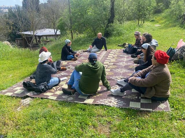 People sitting together on a mat in a grassy clearing