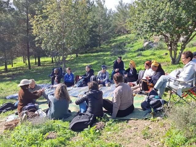 A group seated in a circle beneath trees in a forest clearing